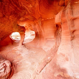 May include: A close-up view of a red sandstone cave with multiple openings. The cave walls are textured and show the layers of rock formation. The light shines through the openings, illuminating the interior of the cave.