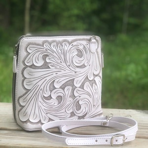 Peut inclure: Sac &agrave; bandouli&egrave;re en cuir blanc avec un motif floral complexe en relief sur le devant. Le sac a une bandouli&egrave;re r&eacute;glable blanche avec une boucle argent&eacute;e.
