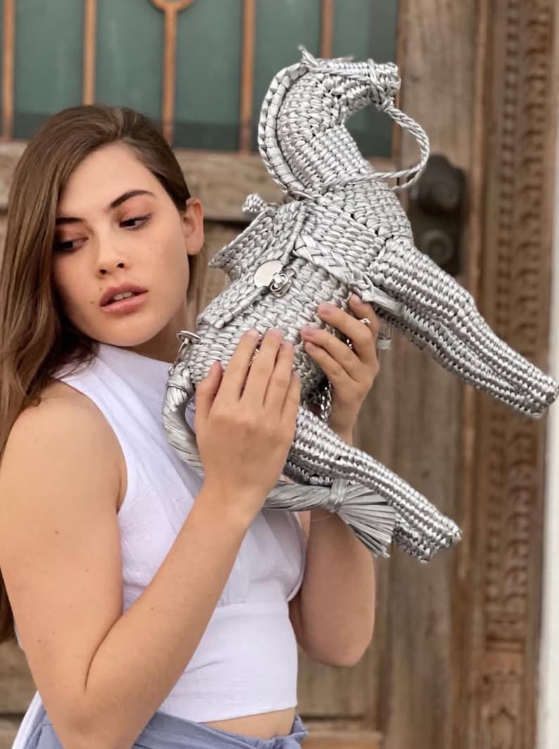 Pu&ograve; includere: Una scultura di cavallo intrecciato argentato con criniera, coda e sella dettagliate. La scultura &egrave; realizzata in un materiale lucido e metallico e presenta un design decorativo. Il cavallo &egrave; tenuto da una persona.