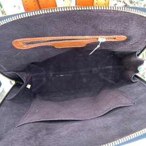 May include: The inside of a brown leather backpack with a zippered pocket. The backpack is lined with a dark brown fabric.