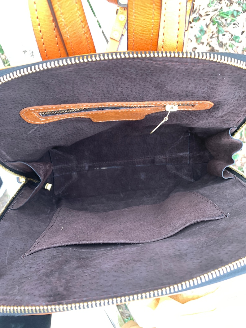 May include: The inside of a brown leather backpack with a zippered pocket. The backpack is lined with a dark brown fabric.