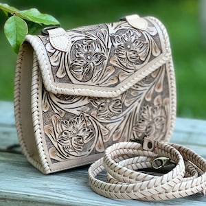 Pode incluir: Uma bolsa de ombro de couro branco com um design floral trabalhado e uma al&ccedil;a tran&ccedil;ada.