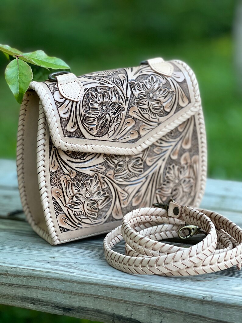 Pode incluir: Uma bolsa de ombro de couro branco com um design floral trabalhado e uma al&ccedil;a tran&ccedil;ada.