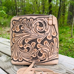 Peut inclure: Un sac &agrave; bandouli&egrave;re en cuir marron clair avec un motif floral. Le sac a une fermeture &eacute;clair et une bandouli&egrave;re r&eacute;glable.