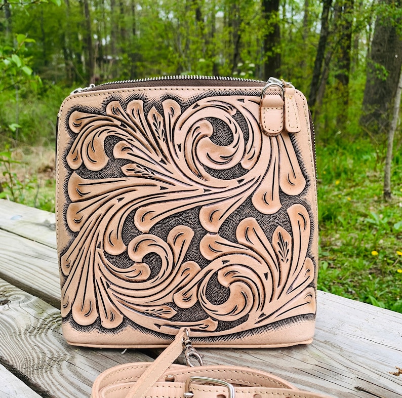Peut inclure: Un sac &agrave; bandouli&egrave;re en cuir marron clair avec un motif floral. Le sac a une fermeture &eacute;clair et une bandouli&egrave;re r&eacute;glable.