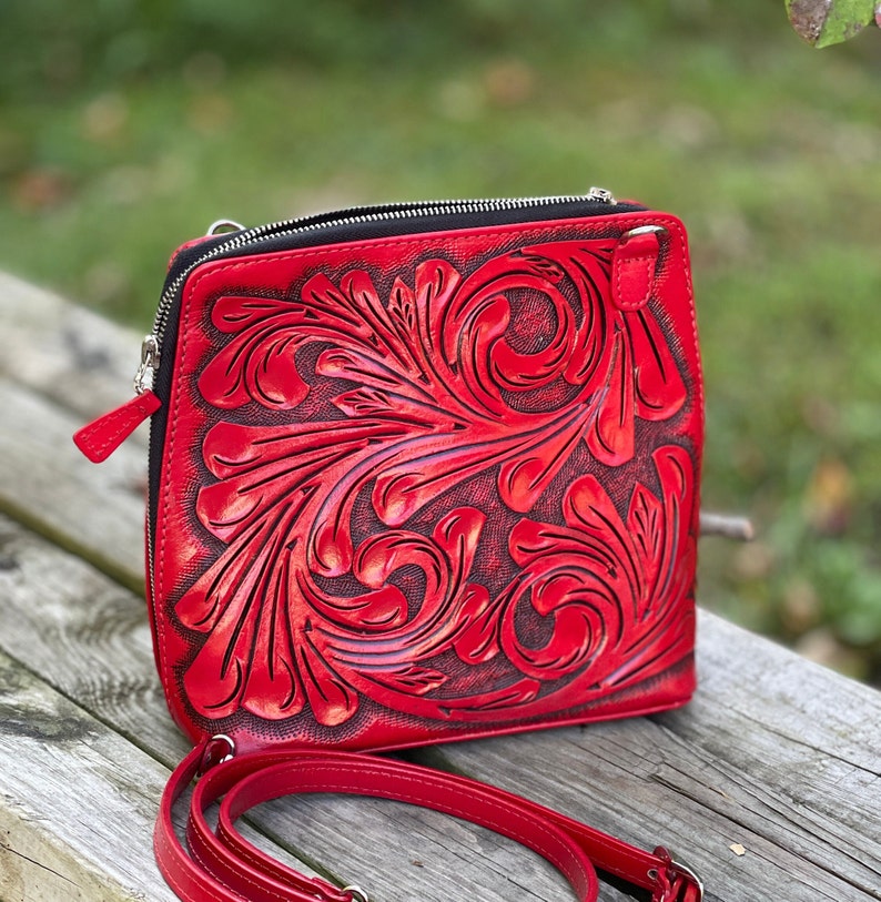 Peut inclure: Un sac &agrave; bandouli&egrave;re en cuir rouge avec un motif floral complexe. Le sac a une fermeture &agrave; glissi&egrave;re et une bandouli&egrave;re r&eacute;glable.