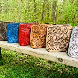Peut inclure: Une rang&eacute;e de six sacs en cuir avec des motifs floraux complexes dans diff&eacute;rentes couleurs, notamment noir, marron, bleu, rouge, beige et blanc. Les sacs sont align&eacute;s sur un banc en bois.