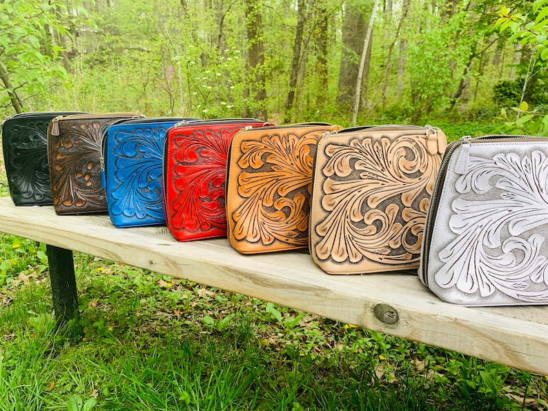 Peut inclure: Une rang&eacute;e de six sacs en cuir avec des motifs floraux complexes dans diff&eacute;rentes couleurs, notamment noir, marron, bleu, rouge, beige et blanc. Les sacs sont align&eacute;s sur un banc en bois.