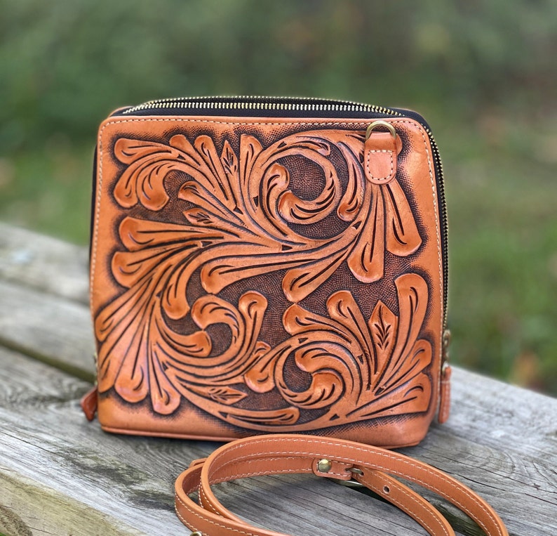 Peut inclure: Un sac &agrave; bandouli&egrave;re en cuir marron avec un motif en relief floral. Le sac a une fermeture &eacute;clair et une longue bandouli&egrave;re r&eacute;glable.