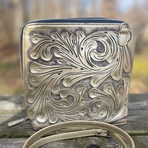 Peut inclure: Un sac &agrave; bandouli&egrave;re en cuir dor&eacute; avec un motif floral complexe. Le sac a une fermeture &agrave; glissi&egrave;re et une longue bandouli&egrave;re r&eacute;glable.