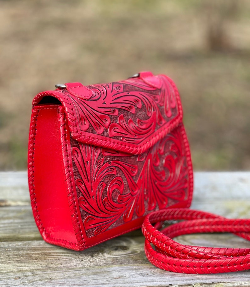 Pode incluir: Uma bolsa de ombro de couro vermelho com um design floral em relevo e uma al&ccedil;a tran&ccedil;ada.