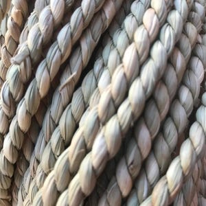 Pu&ograve; includere: Primo piano di una corda fittamente intrecciata con fibre naturali. La corda &egrave; di colore beige chiaro con una superficie strutturata. I fili sono strettamente attorcigliati, creando un aspetto forte e durevole. La corda &egrave; probabilmente utilizzata per scopi decorativi o funzionali.