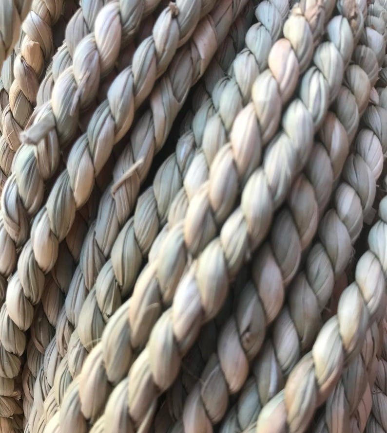 Pu&ograve; includere: Primo piano di una corda fittamente intrecciata con fibre naturali. La corda &egrave; di colore beige chiaro con una superficie strutturata. I fili sono strettamente attorcigliati, creando un aspetto forte e durevole. La corda &egrave; probabilmente utilizzata per scopi decorativi o funzionali.