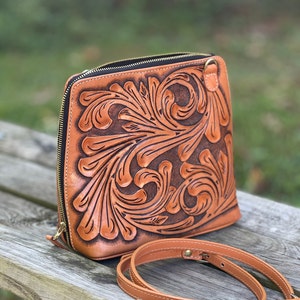 Peut inclure: Un sac &agrave; bandouli&egrave;re en cuir marron avec un motif floral complexe. Le sac a une fermeture &agrave; glissi&egrave;re et une bandouli&egrave;re r&eacute;glable.
