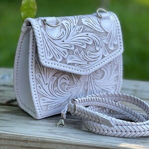 Pode incluir: Bolsa de ombro de couro branco com um design floral intrincado e uma al&ccedil;a tran&ccedil;ada.