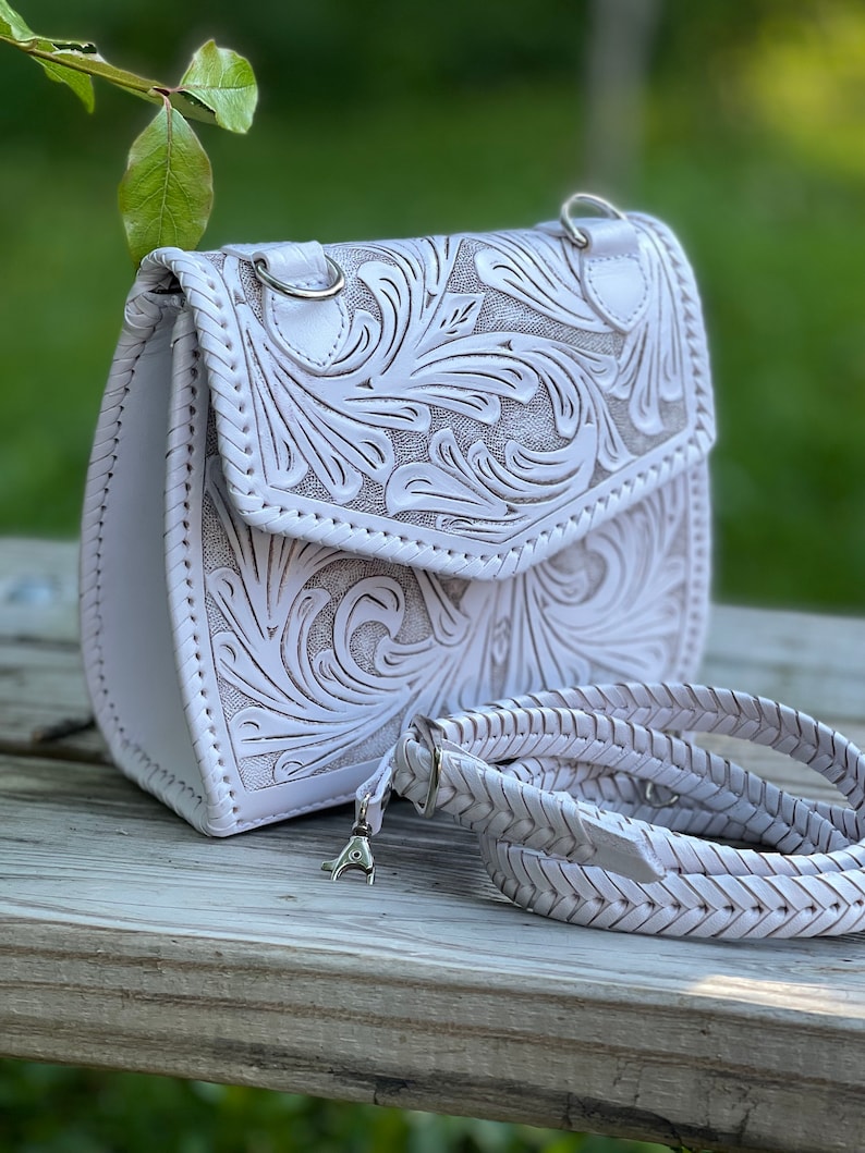 Pode incluir: Bolsa de ombro de couro branco com um design floral intrincado e uma al&ccedil;a tran&ccedil;ada.