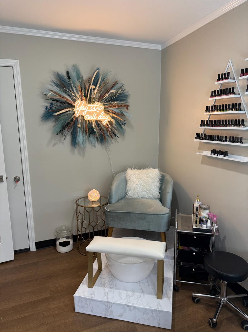 May include: Interior of a nail salon featuring a light blue armchair, foot spa, and a rolling cart with nail supplies. A neon sign reading "Yay it's nail day" is on the wall. A decorative wall hanging is also present.