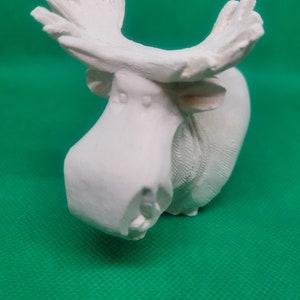 May include: White ceramic moose figurine with a stylized, cartoonish design. The moose has large, pointed ears and a long, curved nose.