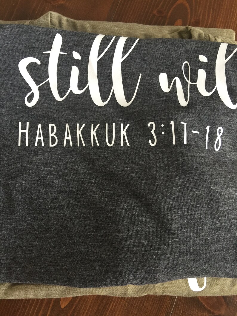 May include: Gray and green t-shirt with the text "still will" and "HABAKKUK 3:17-18" in white.
