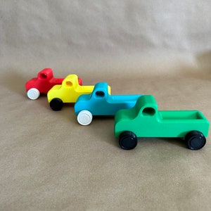 May include: Four wooden toy pickup trucks in a row. The trucks are red, yellow, blue, and green. The trucks have black wheels.