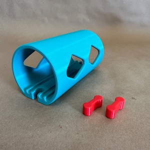 May include: A turquoise blue plastic dog toy shaped like a tube with three cut-out diamond shapes. Two red plastic bone-shaped toys are on a brown surface.