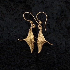 May include: Gold-tone earrings featuring a detailed manta ray design. The earrings have a dangling style with a hook closure.