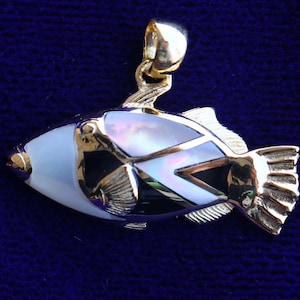Pode incluir: Um pingente de ouro em forma de peixe com incrustações de madrepérola preta e branca. O peixe tem um design detalhado e um laço na parte superior para prender uma corrente.