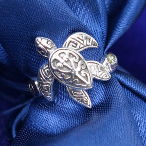 May include: A silver ring with a detailed turtle design. The turtle is facing the right and has a detailed shell and head.