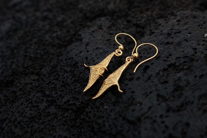 May include: A pair of gold-toned earrings with a manta ray design. The earrings are delicate and have a dangling style.