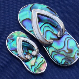 Könnte beinhalten: Zwei silberne Flip-Flop-Anhänger aus schillerndem Abalone-Muschel. Die Anhänger sind hellblau, grün und violett.