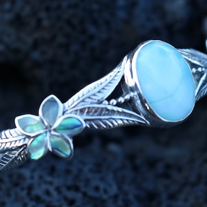 May include: A silver bracelet with a blue oval gemstone and a flower design made of abalone shell.