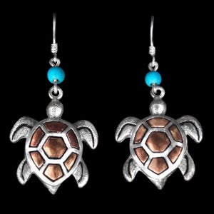 May include: A pair of dangle earrings featuring silver-toned sea turtle charms with copper-colored shell inlays. Each earring is accented with a single round turquoise-colored bead positioned above the turtle charm on a silver-toned hook wire.