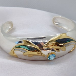 May include: Silver cuff bracelet with two gold dolphins with abalone shell inlay and a blue topaz gemstone.