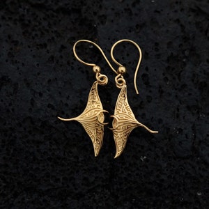 May include: A pair of gold-tone earrings featuring a detailed manta ray design. The earrings are made of metal and have a dangling style.