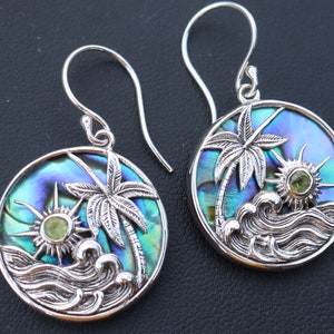 May include: Sterling silver earrings with a blue and green abalone shell design featuring palm trees, waves, and a sun with a green gemstone.