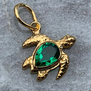 Op de afbeelding: Een gouden schildpad hanger met een groene edelsteen. De schildpad is gedetailleerd met een getextureerde schild en poten.