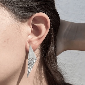 Könnte beinhalten: Ein Paar silberne Dreiecksohrringe mit einer strukturierten Oberfläche.