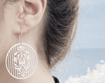 Puede incluir: Pendientes de metal blanco con un diseño circular que presenta un patrón geométrico y rayas.