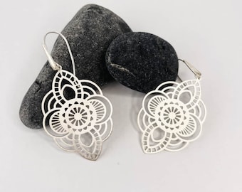 Puede incluir: Un par de pendientes de plata con un diseño delicado y circular. Los pendientes están hechos de metal y tienen un acabado pulido.