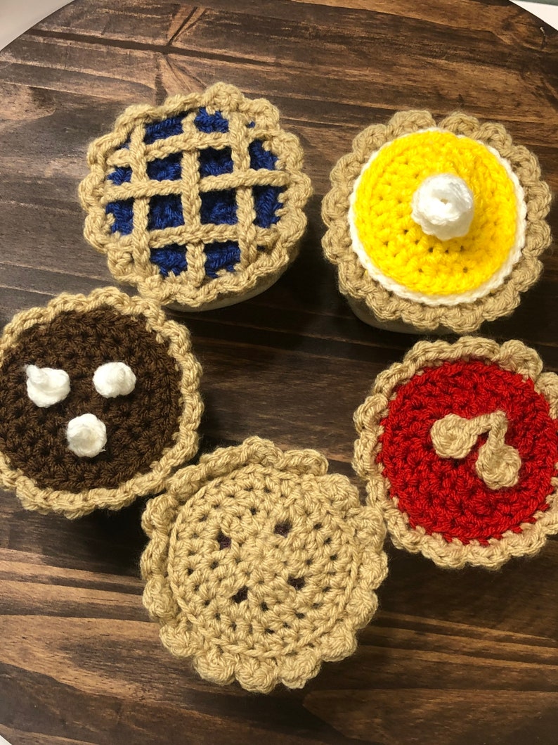 May include: Five crocheted pie decorations in various colors and designs. The pies are brown, blue, yellow, red, and tan.