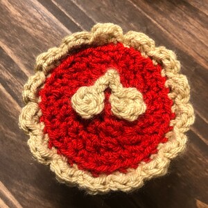 May include: A crocheted cherry pie with a red filling and a tan crust.