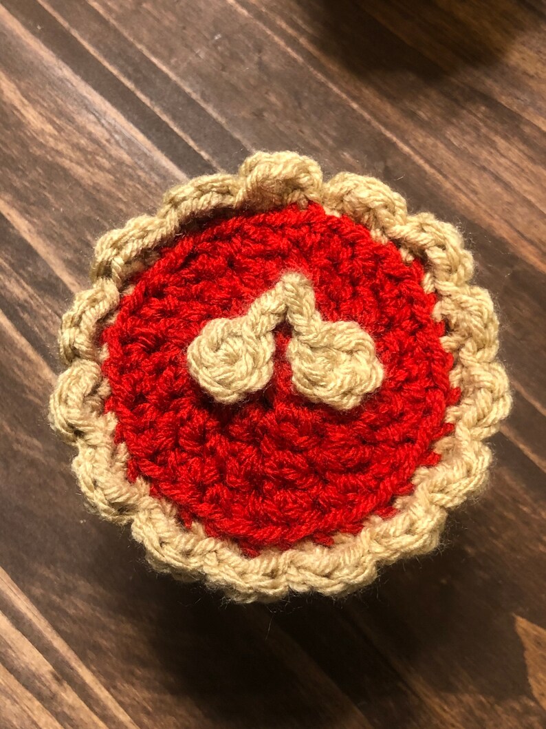 May include: A crocheted cherry pie with a red filling and a tan crust.