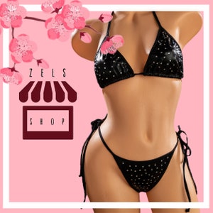 Puede incluir: Bikini negro con pedrer&iacute;a. La parte de arriba es de estilo triangular y la parte de abajo es de corte atrevido. El bikini est&aacute; en un maniqu&iacute; sobre un fondo rosa.