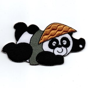 Könnte beinhalten: Ein schwarz-weißes Pandabärchen mit einem braunen Hut und einem lächelnden Gesicht. Der Panda liegt auf der Seite mit den Pfoten unter dem Körper.