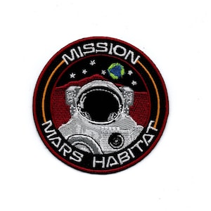 Könnte beinhalten: Ein schwarzer und roter runder Patch mit dem Text "Mission Mars Habitat" in Weiß. Der Patch zeigt einen weißen Astronautenhelm mit schwarzem Visier und eine kleine blaue und grüne Erde im Hintergrund.