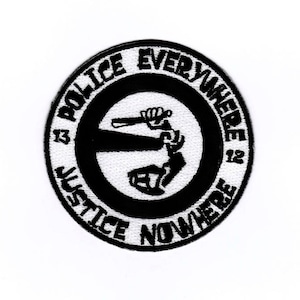 Könnte beinhalten: Schwarz-weiß gestickter Aufnäher mit dem Text "Police Everywhere Justice Nowhere 13 12" in einem Kreis. Die Mitte des Aufnähers zeigt ein stilisiertes Bild einer Hand, die einen Schlagstock hält.