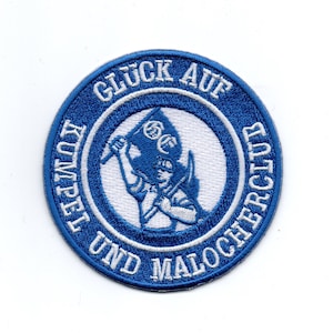 Peut inclure: Patch brodé bleu et blanc avec une figure blanche tenant un drapeau bleu avec trois cercles blancs. Le texte autour de la figure dit "Glück Auf Kumpel und Malocher" en blanc.