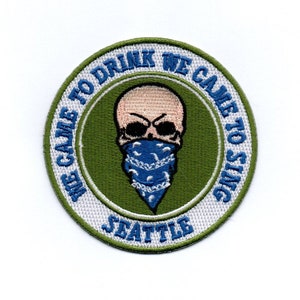 Puede incluir: Un parche circular bordado verde y blanco con una calavera que lleva un pañuelo azul. El texto alrededor de la calavera dice "We Came To Drink We Came To Sing Seattle".