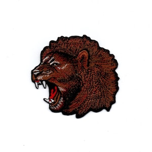 Può includere: Un toppa ricamata di una testa di leone marrone con la bocca aperta e denti affilati. La toppa è su uno sfondo bianco.