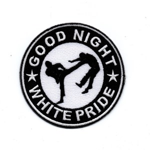 Può includere: Toppa ricamata in bianco e nero con un design circolare. Il cerchio ha il testo "GOOD NIGHT WHITE PRIDE" attorno al bordo con una stella su ogni lato del testo. All'interno del cerchio c'è una silhouette di due persone che combattono.